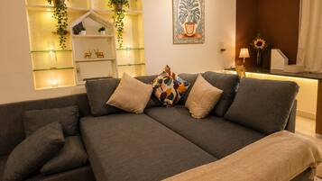 A modern living room with a grey sofa, a beige throw blanket, and a wall-mounted shelf with plants.