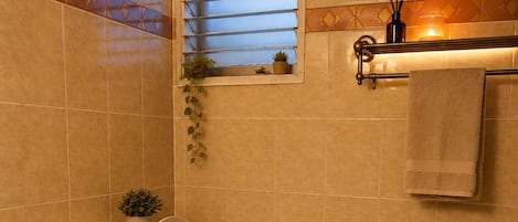A modern bathroom with a toilet, a shower, and a window with blinds.