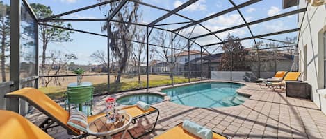 Un espacio exterior cubierto con piscina, sillas de descanso y una mesa con una bebida.