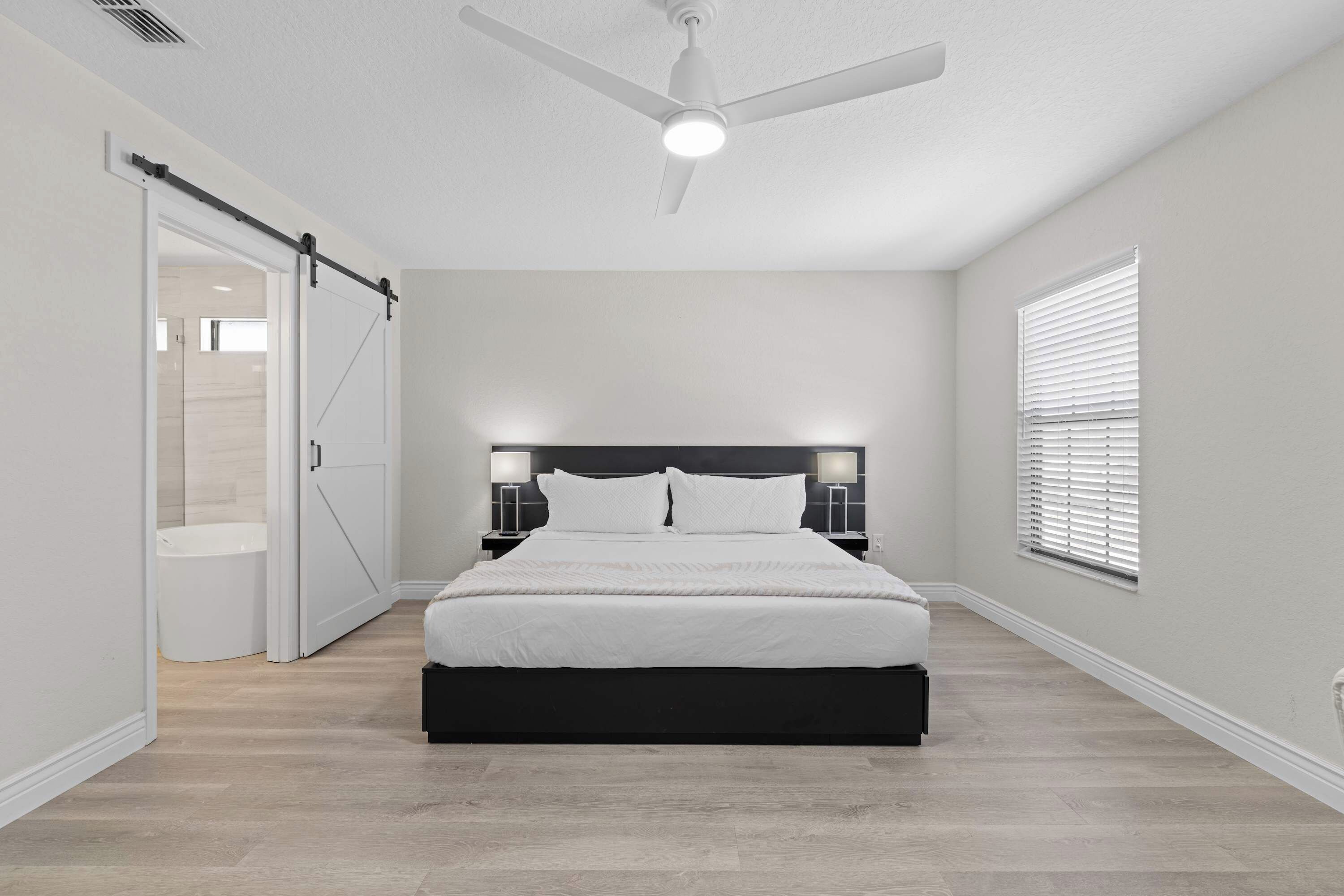 A bedroom with a bed, a ceiling fan, a window with blinds, and a sliding door.
