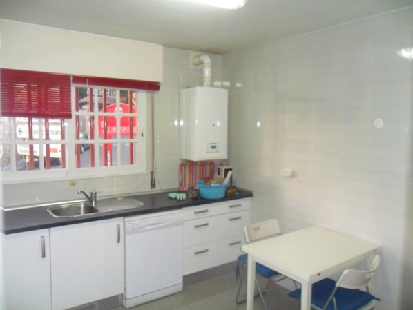 A compact kitchen with white cabinets, a dishwasher, a sink, and a window with red blinds.