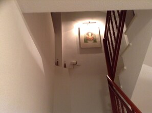 A narrow stairway with a wooden handrail, a wall-mounted light fixture, and a framed picture.