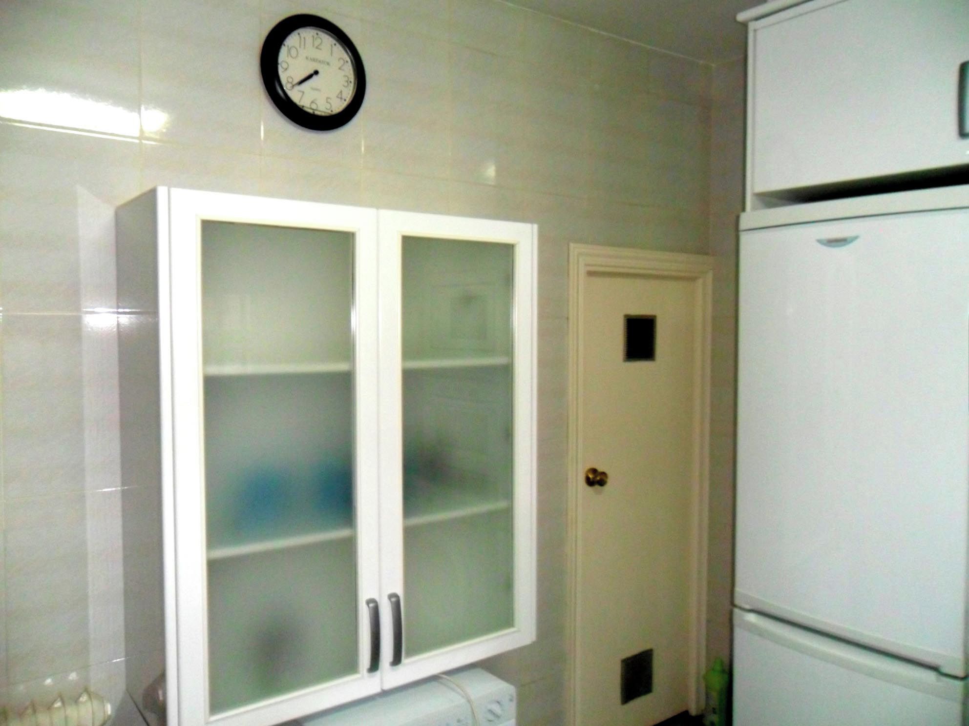 A bathroom with a white cabinet, a clock, and a white refrigerator.