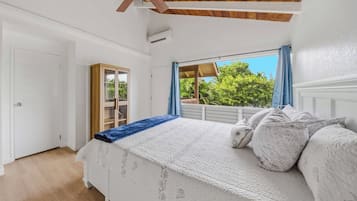 Ein Schlafzimmer mit einem Bett, einem Deckenventilator, einem Fenster mit Vorhängen und Blick ins Grüne.