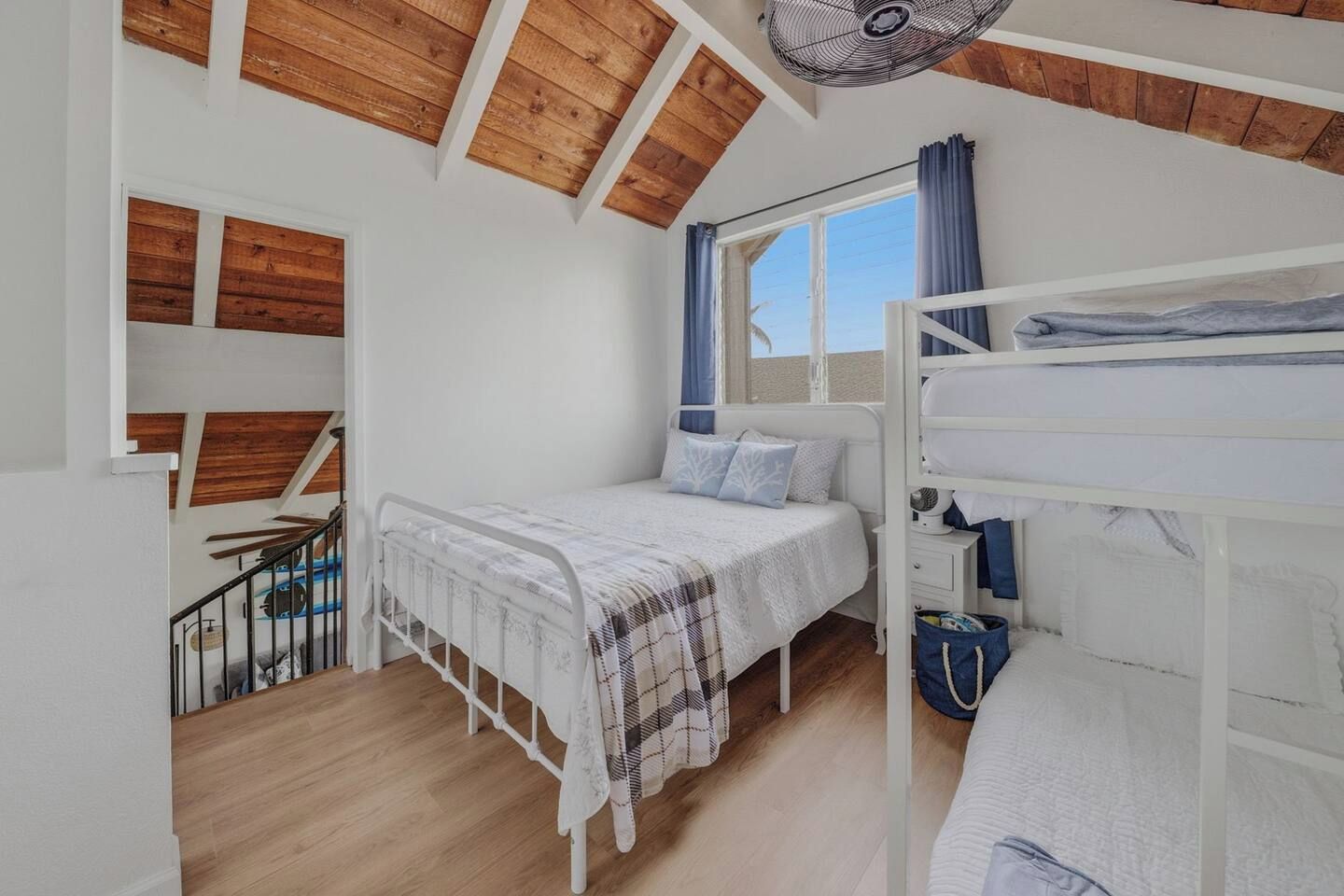 Ein Schlafzimmer mit Etagenbett, einem Einzelbett, einem Fenster mit Vorhängen und einem Ventilator.