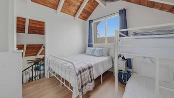 Ein Schlafzimmer mit Etagenbett, einem Einzelbett, einem Fenster mit Vorhängen und einem Ventilator.