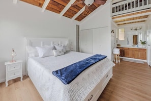 Un dormitorio con una cama grande, una mesita de noche, techo de madera y vistas a una zona de cocina.