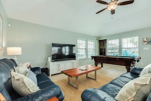 A living room with a sofa, a coffee table, a television, a pool table, and a ceiling fan. - Private Canal Home w/ Boat Dock & Slip, Pool Table, Open Deck (Galveston)