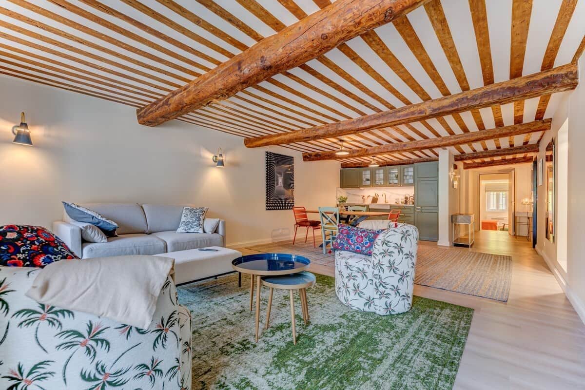 A spacious living area with a high wooden ceiling, a sofa set, a coffee table, and a patterned ottoman.