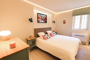 Ein Schlafzimmer mit Bett, Nachttisch, Lampe, Wandbild und einem Fenster.