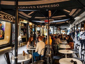 An outdoor café area with tables and chairs, umbrellas, and people dining. - Melbourne 1-bed Apartment Flinders Street (Melbourne)