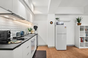 A modern kitchen with white cabinetry, a black countertop, a built-in oven, a microwave, and a refrigerator. - Melbourne 1-bed Apartment Flinders Street (Melbourne)