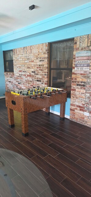 A room with a foosball table, brick wall, and a window.