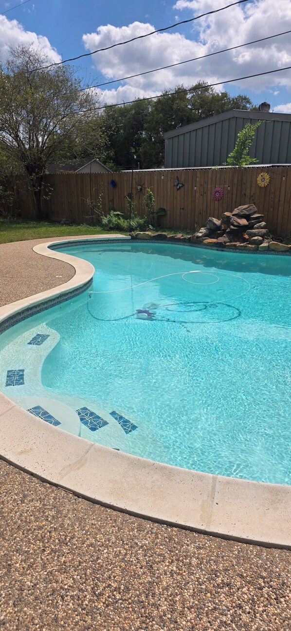 A swimming pool with a pebble border and a wooden fence in the background.