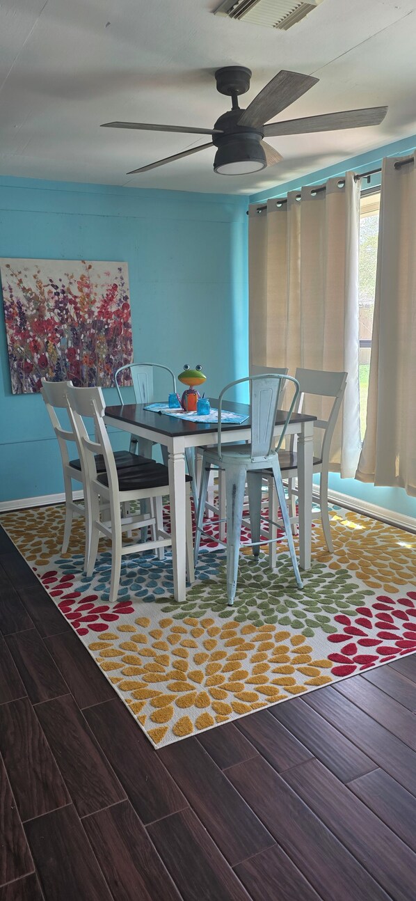 A dining area with a ceiling fan, a table with chairs, and a colorful rug.
