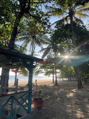 A beach scene with a wooden structure, palm trees, and a clear view of the sea. - Beautiful 3-bedroom apartment,3 Min walk to the Beach,Costambar Puerto Plata,DR (Puerto Plata)