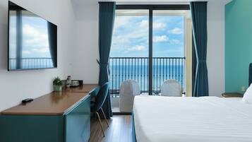 A hotel room with a balcony, a desk, a chair, a bed, and a TV.