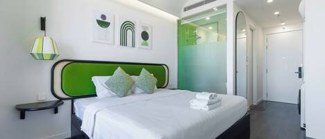 A modern hotel room with a green headboard, white bedding, and a small bedside table.