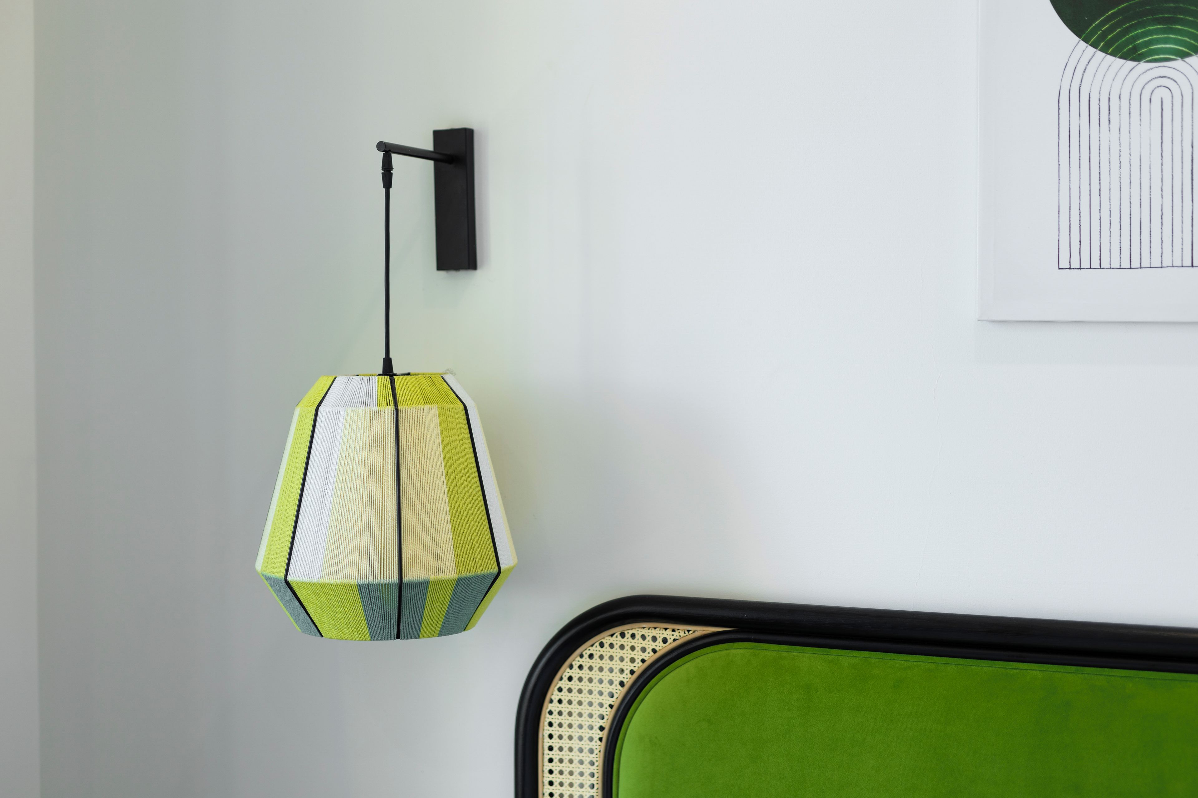 Una habitación con un cabecero tapizado en verde, una lámpara colgante con diseño geométrico y una obra de arte enmarcada en la pared.