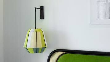 Una habitación con un cabecero tapizado en verde, una lámpara colgante con diseño geométrico y una obra de arte enmarcada en la pared.