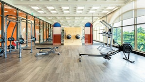 Une salle de sport équipée de machines de cardio, de postes d’entraînement en musculation et de grandes fenêtres donnant sur un espace verdoyant.