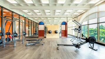 A gym with cardio equipment, weightlifting stations, and large windows offering views of greenery.