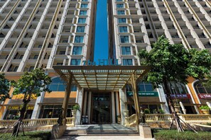A hotel entrance with a central blue stripe, multiple floors, and surrounding shops. - The Clound Apartment Hillside Phu Quoc (Phu Quoc)