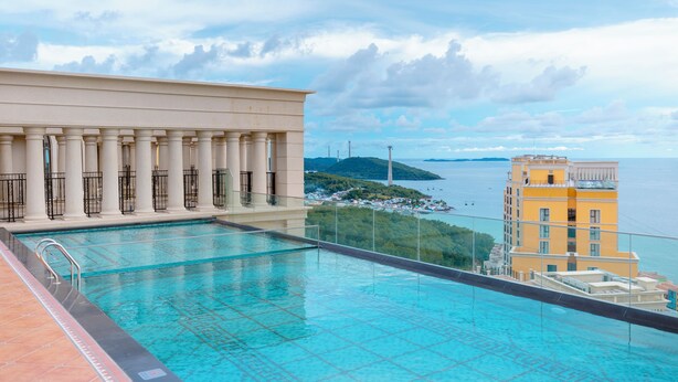 Une piscine sur le toit offrant une vue sur la mer et un bâtiment orné de colonnes.