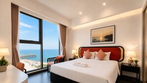 Un cuarto de hotel con un ventanal grande, una cama con sábanas blancas, dos lámparas de noche y un cuadro en la pared.