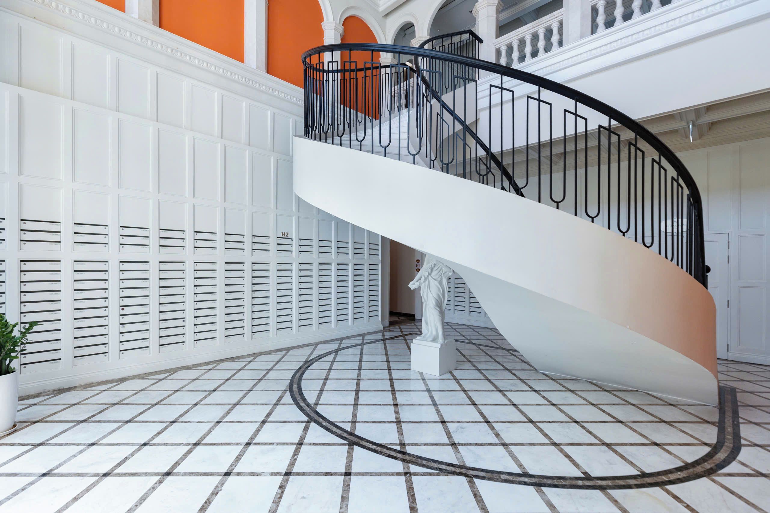 A white spiral staircase with a black railing inside a building with white walls and a tiled floor.