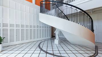 A white spiral staircase with a black railing inside a building with white walls and a tiled floor.