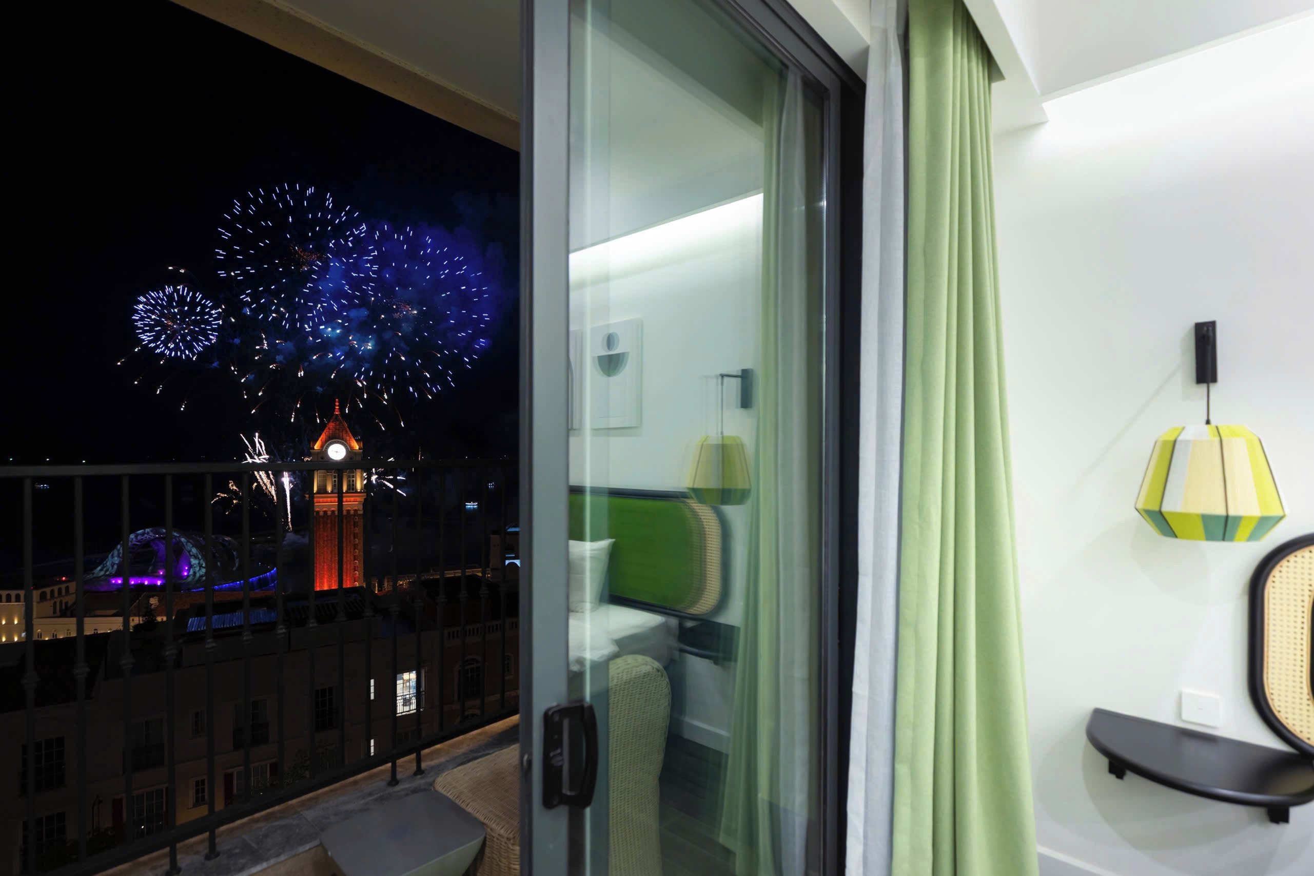 Un balcón con vistas a fuegos artificiales, una torre de reloj y un edificio con ventanas iluminadas.