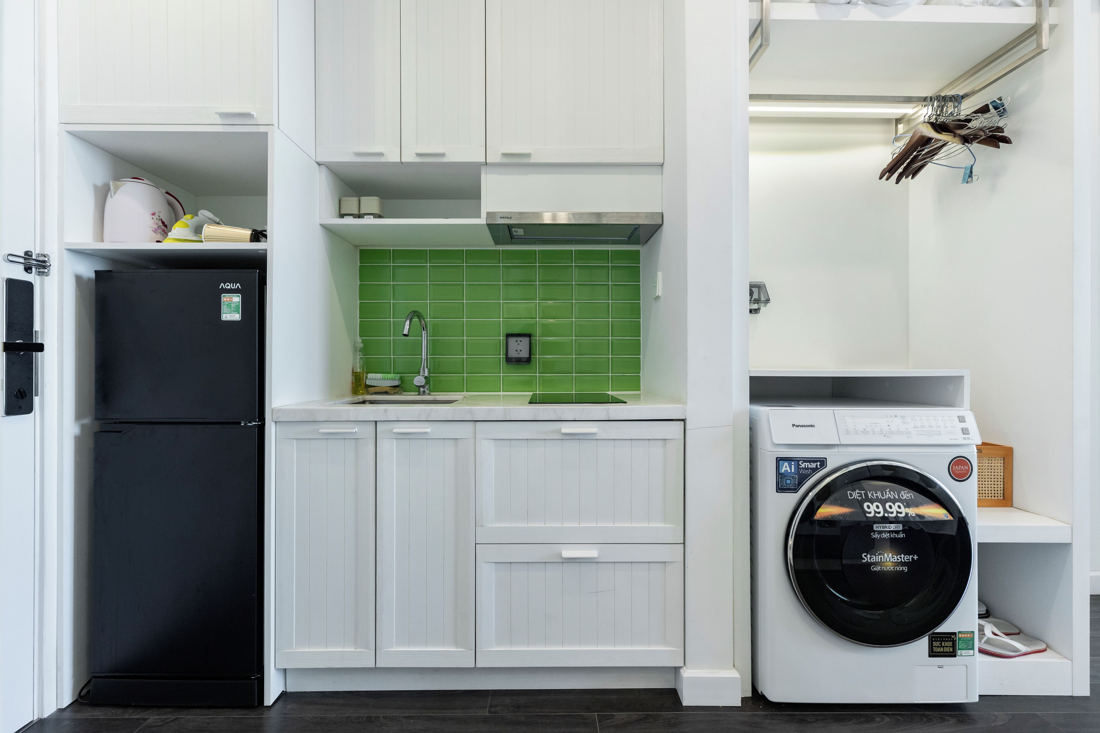 A compact kitchen with white cabinets, a black refrigerator, a green tiled backsplash, and a front-loading washing machine.