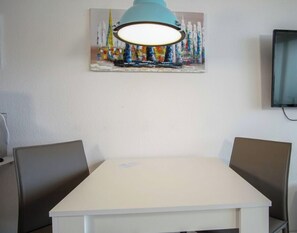 Ein Essbereich mit einem weißen Tisch, vier Stühlen, einer blauen Pendelleuchte und einem Bild an der Wand.