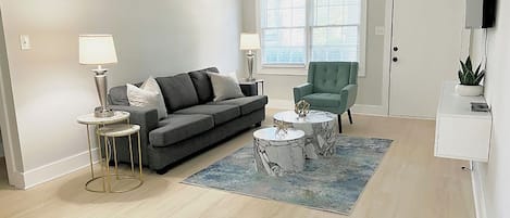A living room with a grey sofa, two side tables, a green armchair, and a marble coffee table.
