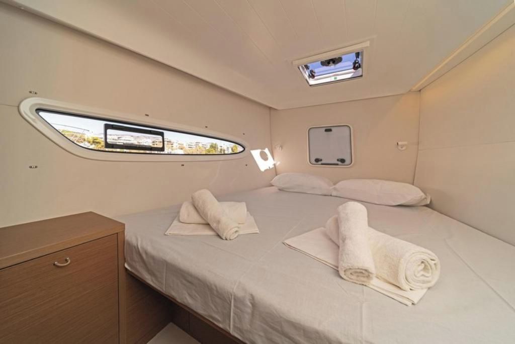 A compact bedroom with a single bed, a small bedside table, a window with a view, and a built-in TV.