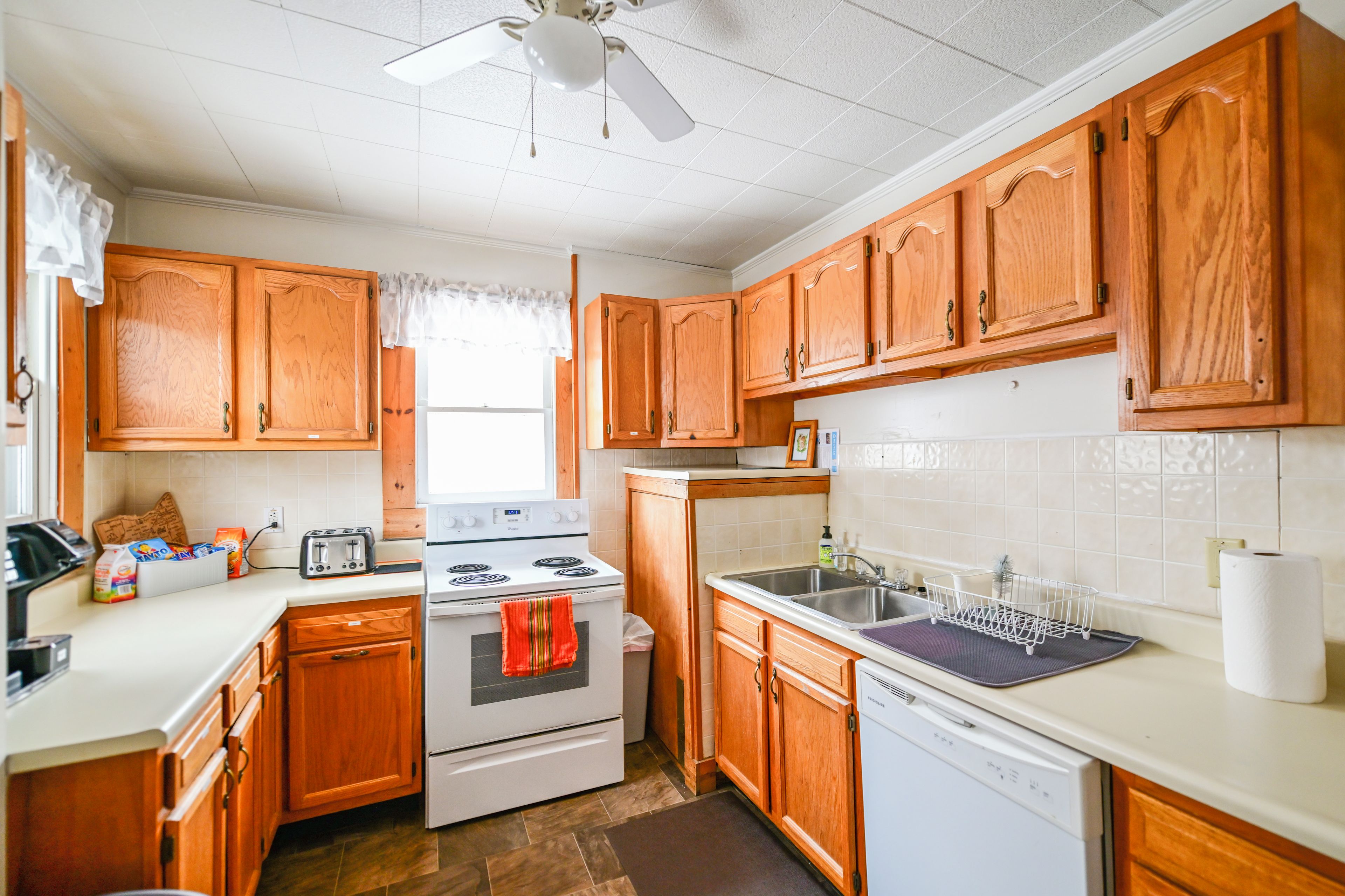 A kitchen with wooden cabinets, a white stove, a sink, and a ceiling fan.