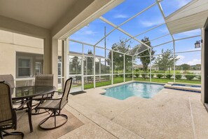 A covered outdoor area with a pool, a table with chairs, and a view of a residential neighborhood. - Perfect Family Escape, Pool, Themed Rooms (Kissimmee)