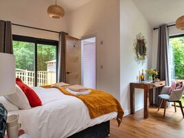 Un dormitorio con cama, escritorio y silla. Hay una ventana con vista a la vegetación.