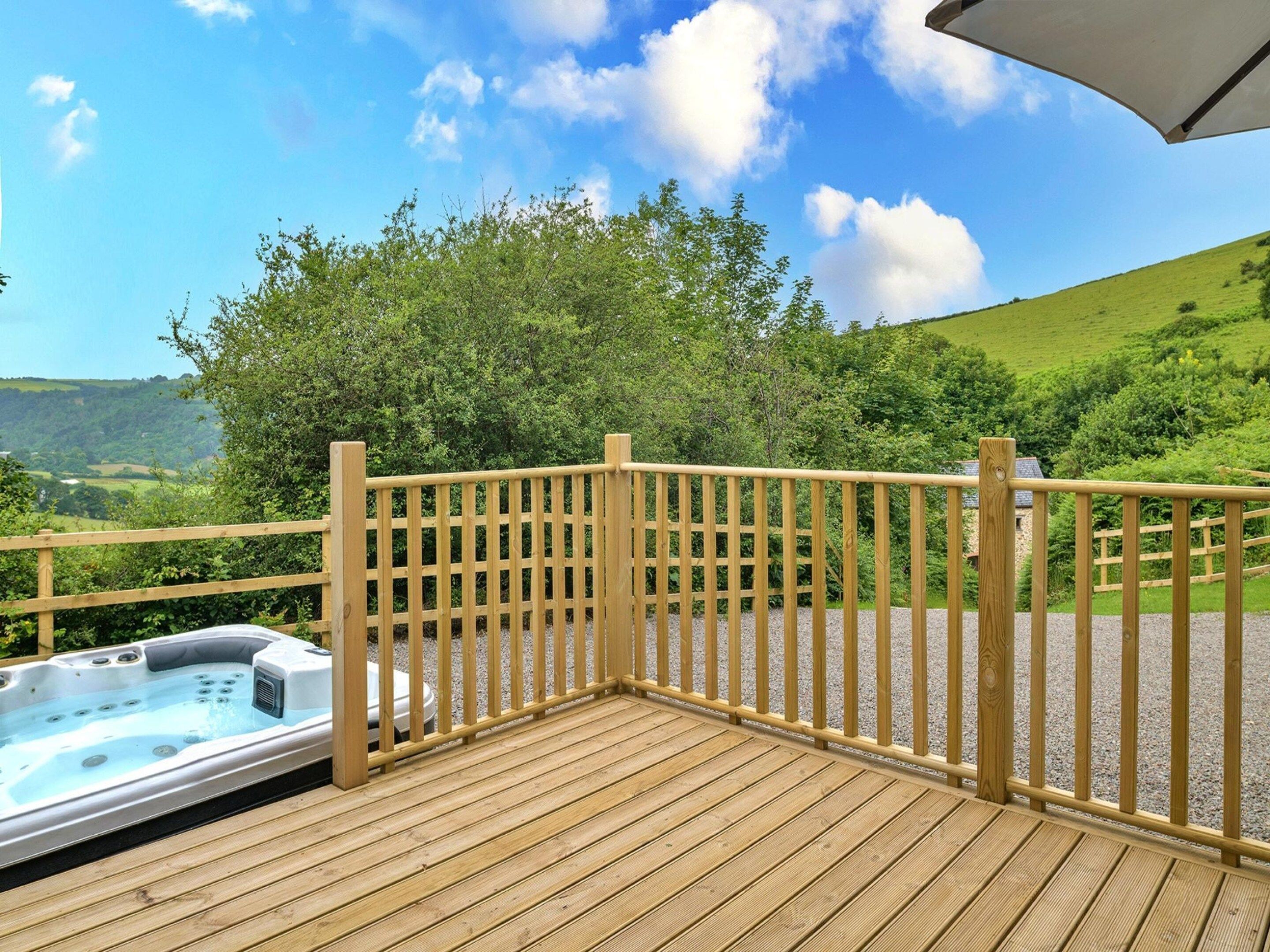 A wooden deck with a hot tub and a view of a green landscape.