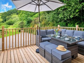 Una terraza con mesa y asientos, rodeada por una valla de madera y abundante vegetación.