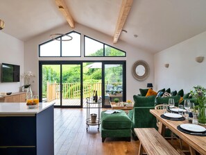 A spacious living area with a wooden ceiling, a large sliding glass door leading to a deck, and a dining table set for two. - Luxury Barn With Private Hot Tub (Ilfracombe)