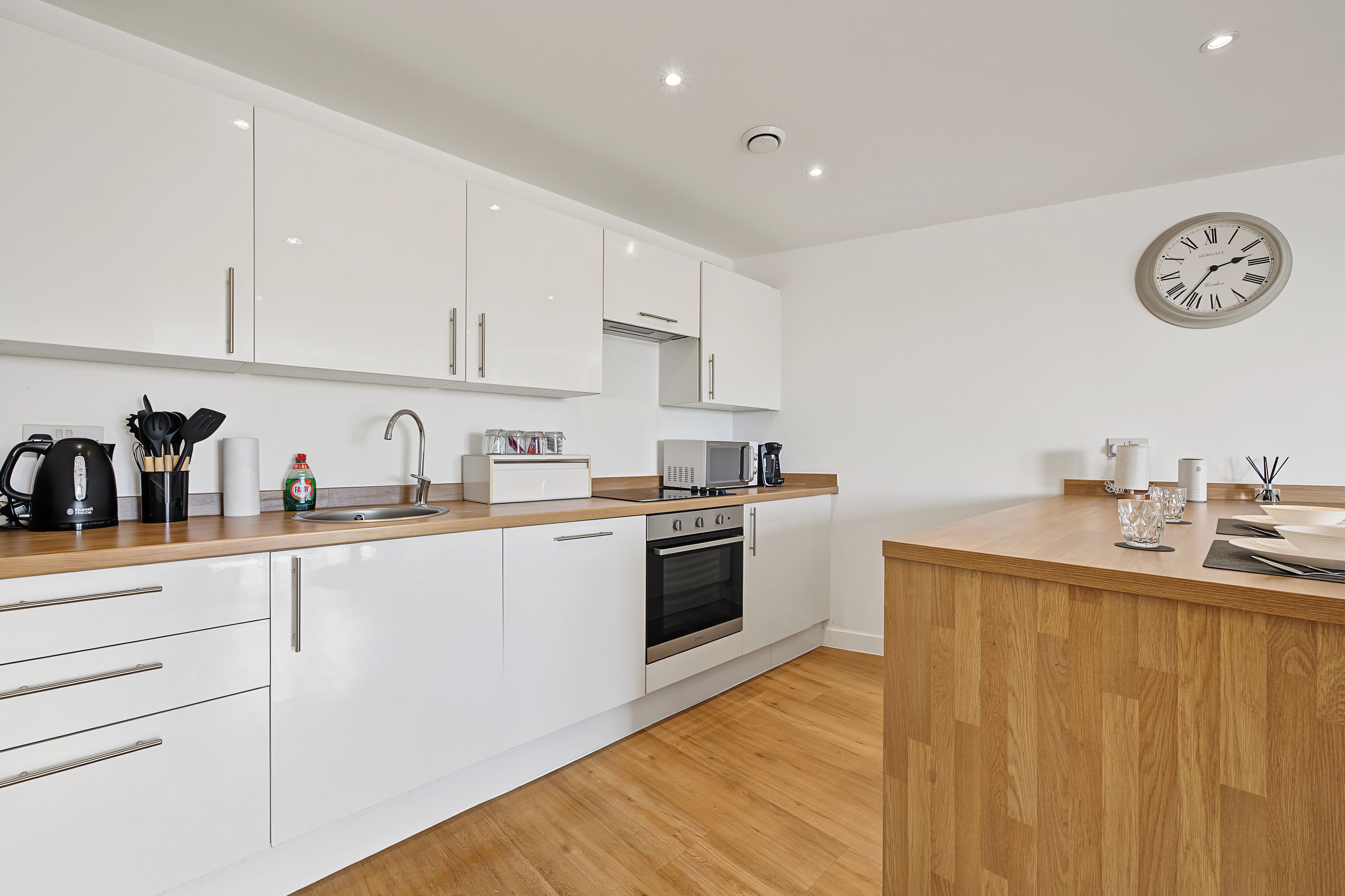 A modern kitchen with white cabinetry, a wooden countertop, stainless steel appliances, and a wall clock.