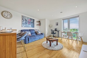 Ein modernes Wohnzimmer mit einem blauen Sofa, einem Holztisch und einem großen Fenster mit Blick auf Grünflächen.