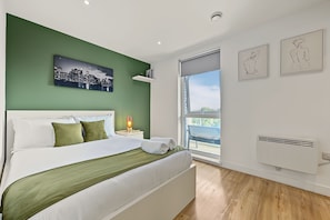 A modern bedroom with a bed, green walls, a cityscape painting, and artwork. - City Centre 2BR • Workspace • Gym • Parking Spot (Manchester)