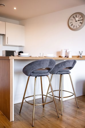 A modern kitchen with two bar stools, a wooden countertop, and a wall clock. - City Centre 2BR • Workspace • Gym • Parking Spot (Manchester)