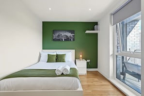Ein modernes Hotelzimmer mit einem Bett, grünen Wänden, einem Stadtbildgemälde, einer Nachttischlampe und einem Fenster mit Blick auf ein Gebäude.