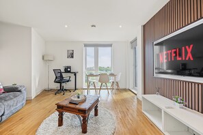 A modern living room with a wooden coffee table, a grey sofa, and a white armchair. A large window provides a view of the outdoors. - City Centre 2BR • Workspace • Gym • Parking Spot (Manchester)