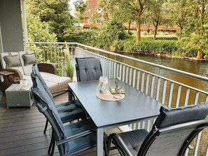 An outdoor seating area with a table and chairs, overlooking a river and greenery. - 50.0.s Waterkant (Wangerland)