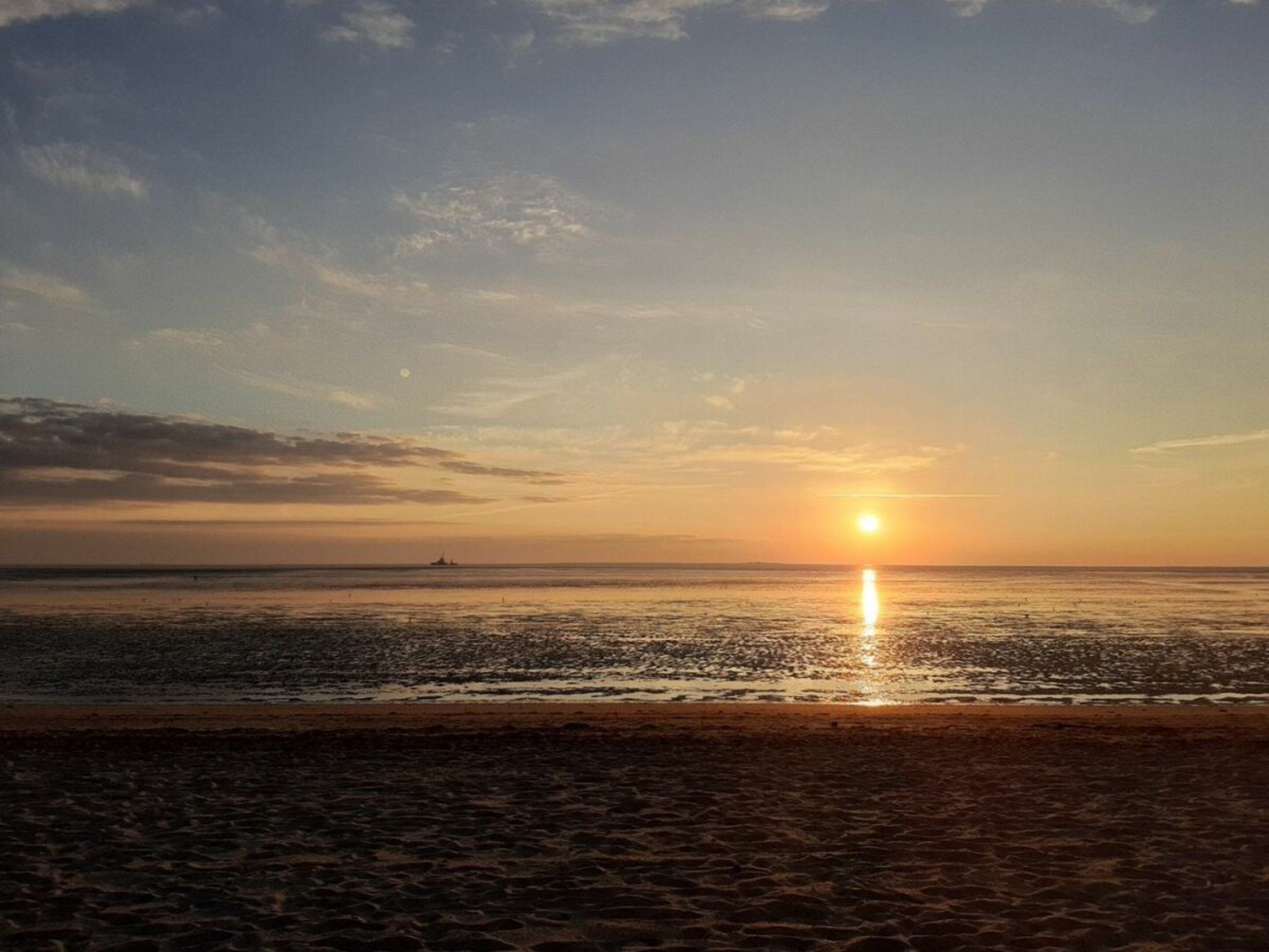Ein Strand bei Sonnenuntergang mit ruhiger See und klarem Himmel.